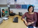 Asian woman wearing glasses sat at a desk with a computer monitor showing plastic displays