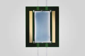 Photo of the Lightmatter device. A long bluish-grey rectangle flanked by thinner gold rectangles is mounted on a larger black rectangle. Wires lead in and out of the device.