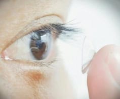 A person holding a small transparent circular-shaped object on their finger near their eye