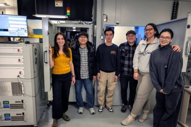 Synchrotron in a closet Six people stand side-by-side in a laboratory in front of a large device that resembles a 5-foot-tall refrigerator with microscope equipment inside the top drawer