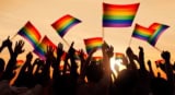Silhouetted crowd at sunset waving Pride flags