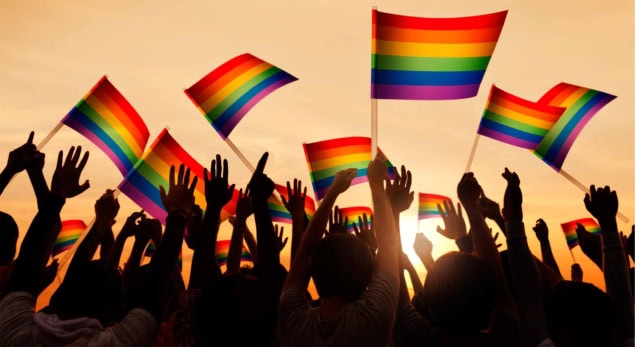 Silhouetted crowd at sunset waving Pride flags Silhouetted crowd at sunset waving Pride flags