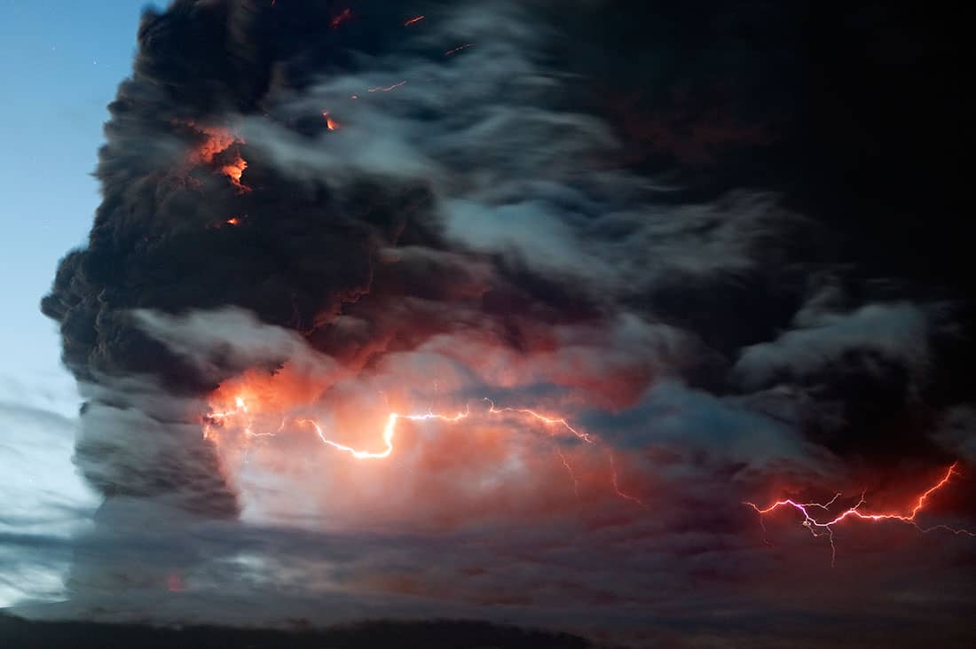 A band of lightning through thick black clouds venting from a volcano