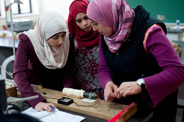 Three women wearing hijab doing a practical physics experiment in a classroom