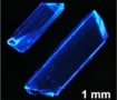 Crystals emitting deep-blue light. A scale bar at the bottom indicates that the crystals are millimetre-scale