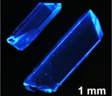 Crystals emitting deep-blue light. A scale bar at the bottom indicates that the crystals are millimetre-scale