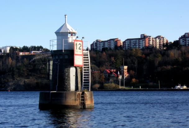 Photo of a lighthouse on a small rock in a bay with the coastline clearly visible close behind
