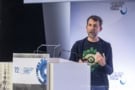 Photo of David Silver standing in front of a podium. He's dressed informally, in a black t-shirt and hoodie