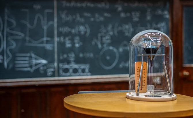 A bell jar covers a funnel containing dark viscous material, a thermometer and a petri dish