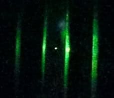 Image of a single nanoparticle made of glass confined in an optical potential created with a focused laser beam. The nanoparticle is a speck of white near the centre of the photo, while the laser beams appear as vertical streaks of green light