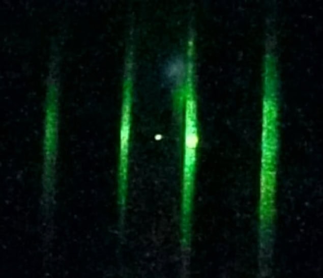 nanoparticle-squeezing Image of a single nanoparticle made of glass confined in an optical potential created with a focused laser beam. The nanoparticle is a speck of white near the centre of the photo, while the laser beams appear as vertical streaks of green light