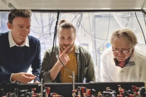 Photo of three men standing behind an optical table