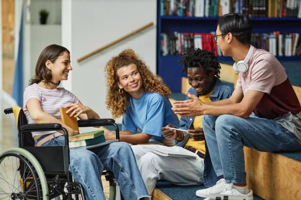 Four students in a university library. One is in a wheelchair and they all have different ethnicities