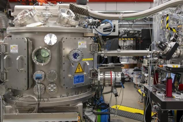 Photo of the IC2 interaction chamber of the HED experimental station at the European XFEL. It's a large metal vacuum chamber with various ports and hoses coming out of it. A strip of yellow caution tape is visible on the floor in the background