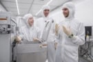 Photo of three researchers in white clean room gear, pictured in a laboratory