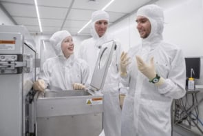Photo of three researchers in white clean room gear, pictured in a laboratory