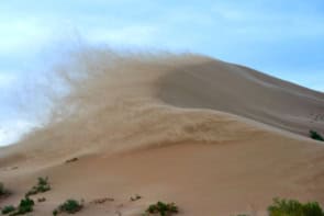 Desert dune with large amount of sand blown up into the air on one side