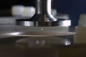 Photo of a speaker, which resembles a metallic plunger, suspending a tiny sphere of silica above a silica plate