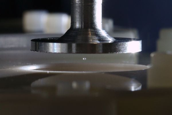Photo of a speaker, which resembles a metallic plunger, suspending a tiny sphere of silica above a silica plate