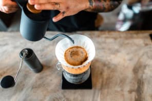 Pouring water from a small black kettle onto coffee in a filter over a glass jug