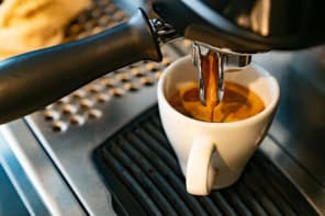 Coffee pouring out of an espresso machine into a small white cup