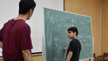 Teacher oversees a pupil drawing on a blackboard