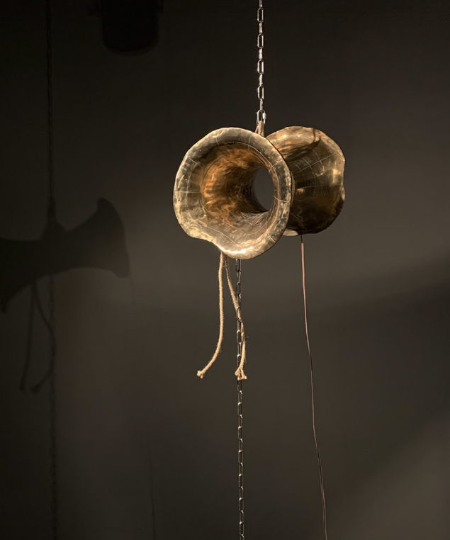 Photo of a suspended bronze sculpture shaped roughly like a wormhole