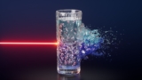 Conceptual image showing a bright neon red laser beam striking a glass of water. Inside the water glass are little ball-and-stick models of water molecules. The glass is divided into dark and light blue regions, representing the two liquid phases of supercooled water. On the side of the glass opposite the laser beam, the water is bursting outward.