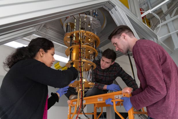 Three people in a lab handling a quantum refrigeration device