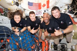 Four astronauts floating in a space capsule holding thumbs up and smiling