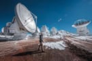 Several large telescopes on a snowy mountain plateau with a person walking past in the foreground