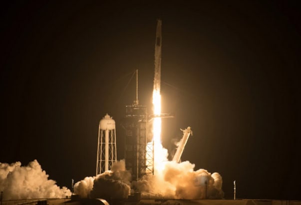 Photo of a rocket launch taken at night, with the flames from the rocket illuminating its surroundings in yellowish white light