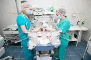 Two medical wearing scrubs either side of an incubator with two premature babies inside