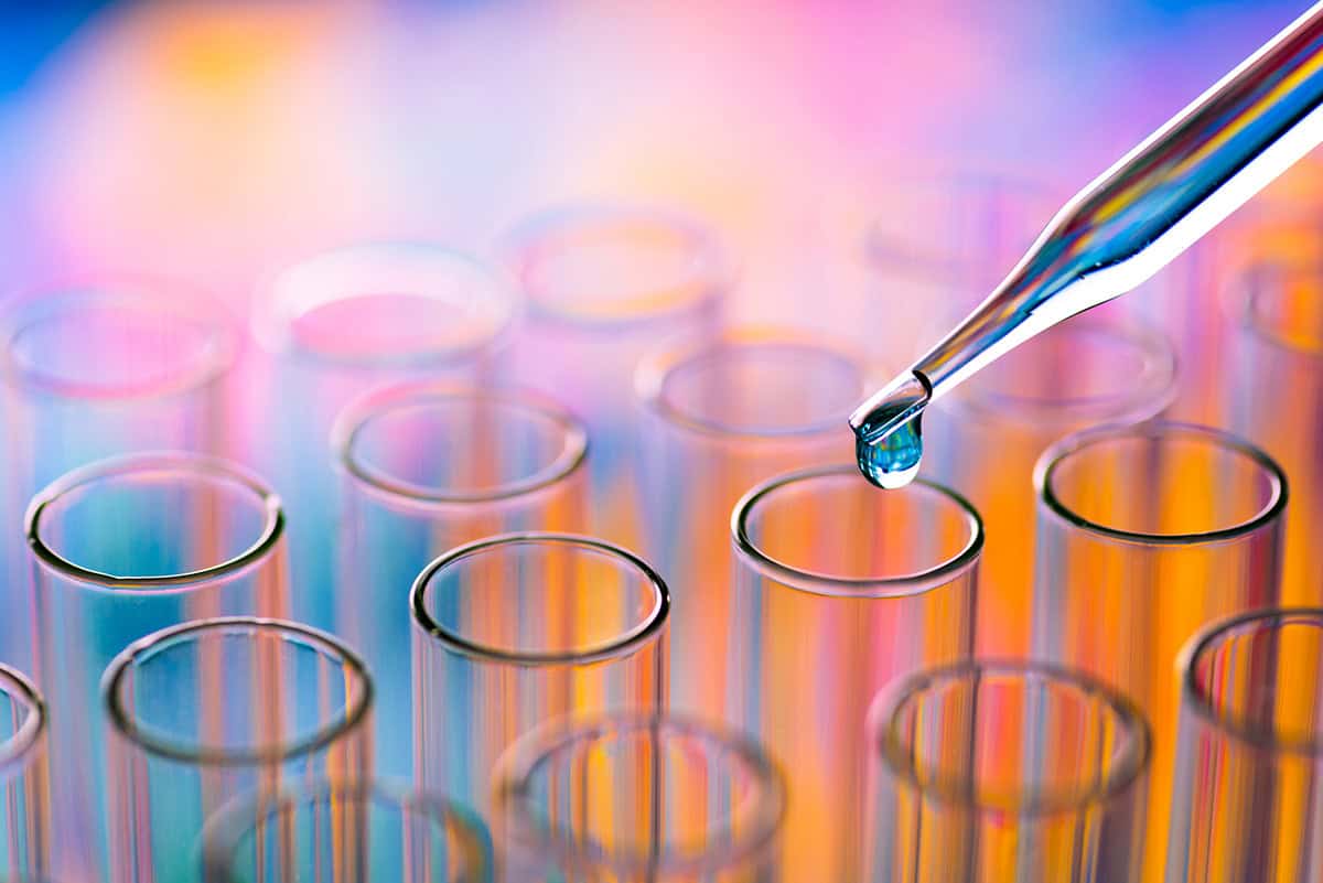 Rows of glass test tubes and a pipette releasing a droplet of liquid into one