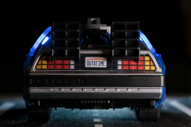 A photo of a Playmobil model of the Delorean used as a time machine in the film Back to the Future. The car has a California licence plate reading "OUTATIME" and looks like it's on a real road.