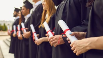 Row of university graduates in caps and gowns, holding their degree certificates