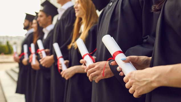 Row of university graduates in caps and gowns, holding their degree certificates