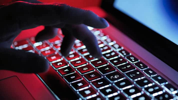Hand typing on a laptop keyboard in low lighting