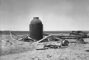Bottle-shaped steel tank in the desert surrounded by a mess of wood and other debris