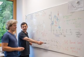 Two scientists in front of a white board covered with diagrams