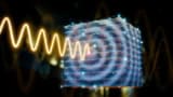 Illustration showing a yellow sinusoidal wave coming in from the left side of the image and impinging on a cube with a rippling interference pattern on its nearest face
