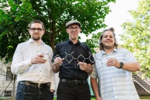 Three men holding a model of a carbon-based model. They're standing outside and there's a tree in the background