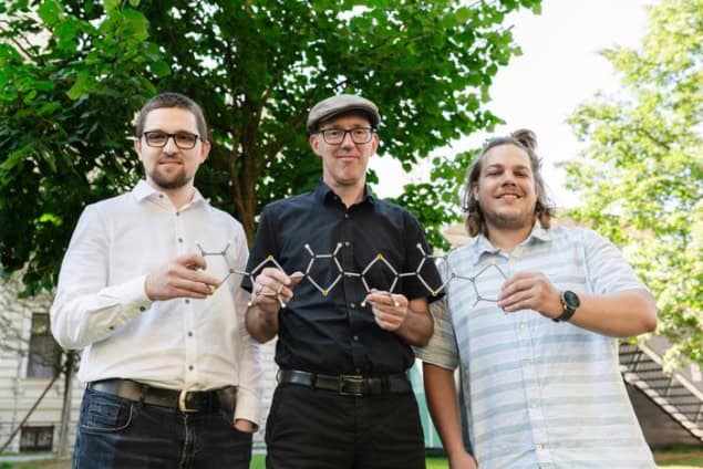 Three men holding a model of a carbon-based model. They're standing outside and there's a tree in the background