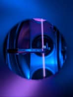 A purplish laser beam passing through a small vial, viewed through a port in a vacuum system