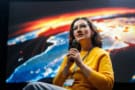 Woman speaking into a microphone on stage in front of a large space photo