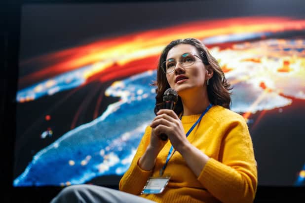 Woman speaking into a microphone on stage in front of a large space photo