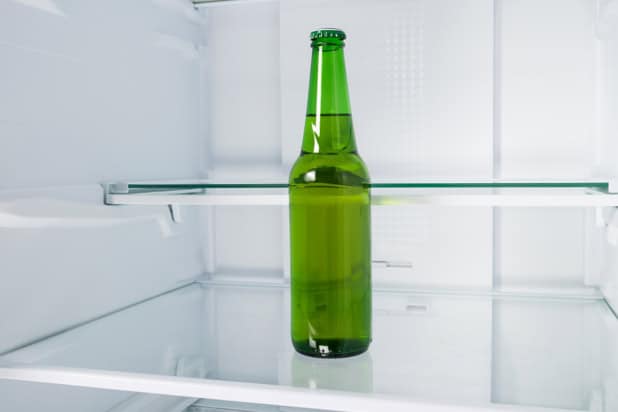 A green glass bottle mostly full of amber liquid sitting in an otherwise empty fridge