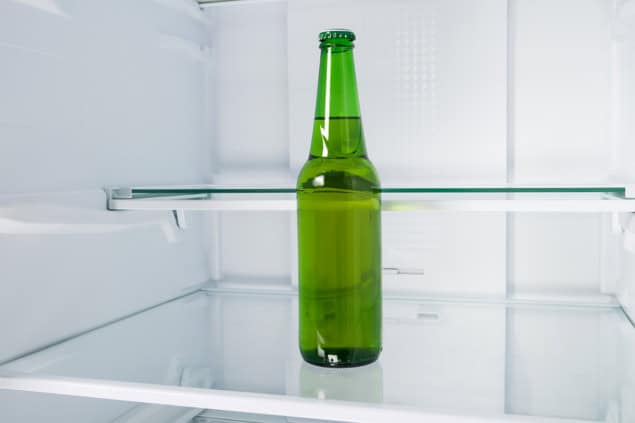 A green glass bottle mostly full of amber liquid sitting in an otherwise empty fridge